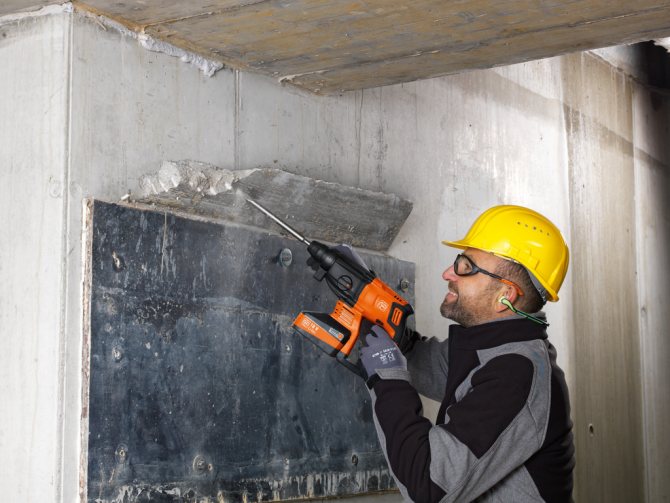 Рабочий забивает бетонную стену перфоратором с долотом